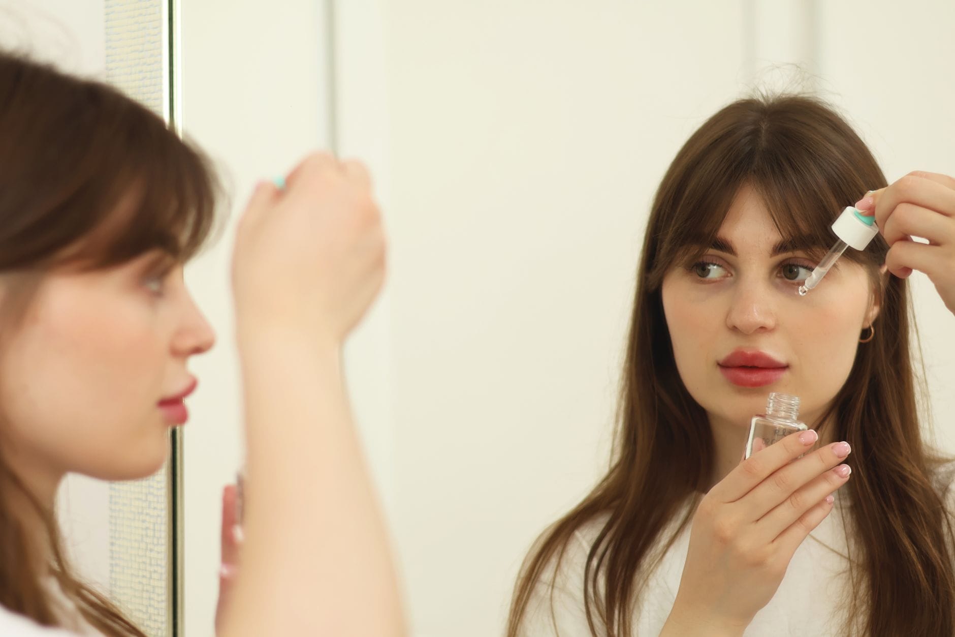 Młoda kobieta nakłada serum do twarzy przed lustrem w łazience
